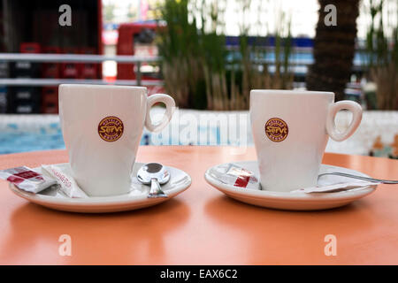 Tasses à café avec soucoupe cuillère à café et biscuits sur une table de couleur orange des paquets de sucre Banque D'Images