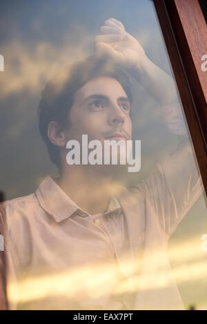 Man looking out fenêtre d'hôtel au coucher du soleil Banque D'Images