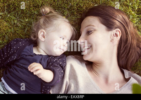 Mère et bébé girl lying on grass, smiling at each other Banque D'Images