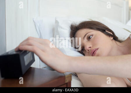 Femme au lit en appuyant sur le bouton snooze réveil Banque D'Images