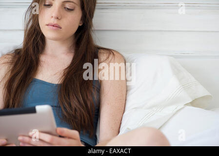 Woman sitting in bed using digital tablet Banque D'Images