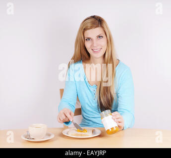 Jeune femme répandre marmelade sur son toast à la table du petit déjeuner Banque D'Images