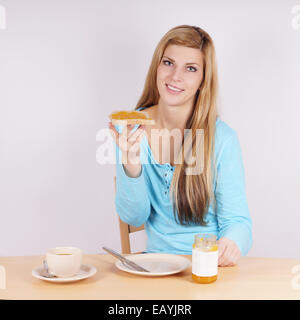 Jeune femme qui mange son petit-déjeuner avec du pain grillé, de la confiture et du café Banque D'Images