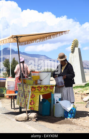 Femme debout tenant un stand de boissons au seau avec un verre de quisa ou KISA (pêche) déshydratés dans Kasani, Bolivie Banque D'Images