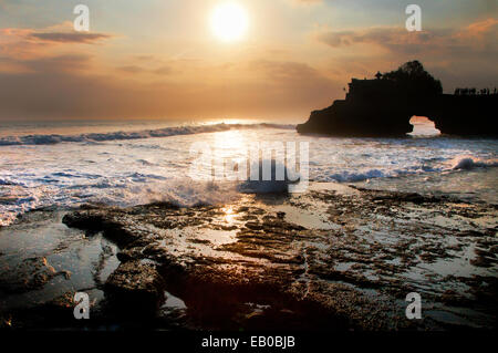 Trou dans le mur, un rocher naturel arch en raison de l'usure de la pierre calcaire au temple de Tanah lot à Bali. caractéristique côtière au coucher du soleil à marée montante et sun Banque D'Images