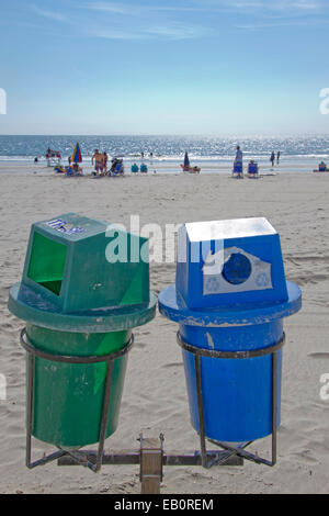 Deux bacs de recyclage au premier plan sur une plage propre avec le soleil par la mer au loin Banque D'Images