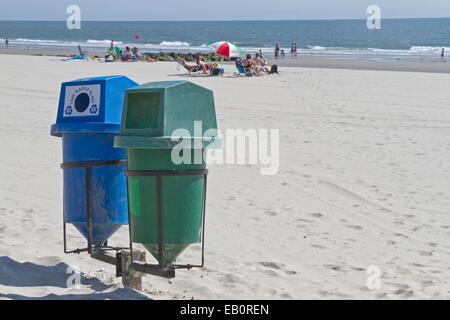 Deux bacs de recyclage au premier plan sur une plage propre avec le soleil par la mer au loin Banque D'Images