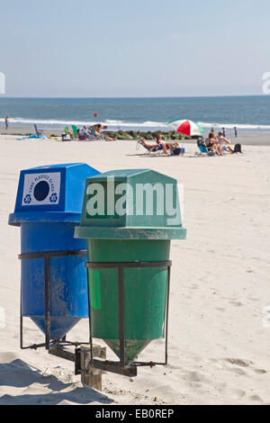 Deux bacs de recyclage au premier plan sur une plage propre avec le soleil par la mer au loin Banque D'Images