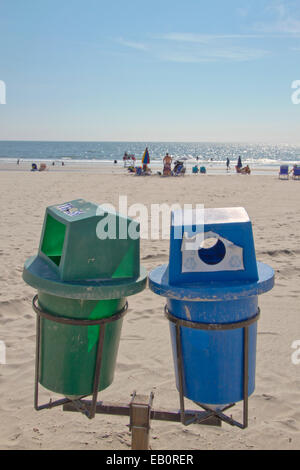 Deux bacs de recyclage au premier plan sur une plage propre avec le soleil par la mer au loin Banque D'Images