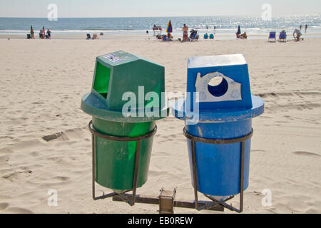 Deux bacs de recyclage au premier plan sur une plage propre avec le soleil par la mer au loin Banque D'Images