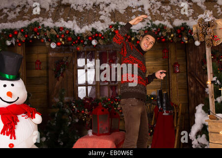 Homme portant un chandail et patins tenant en face de Log Cabin en hiver Banque D'Images