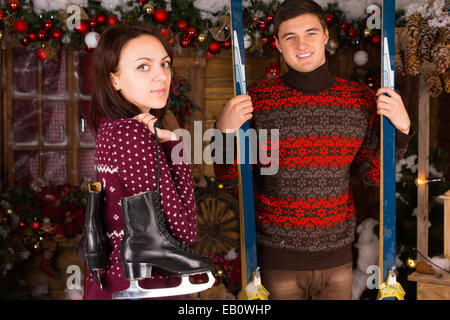 Couple Wearing Pulls Holding skis et patins standing in front of Log Cabin en hiver Banque D'Images