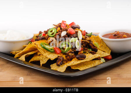 Le piment et le fromage Cheddar frais Nacho plateau avec tomates, oignons, piment jalapeño, crème sure et Salsa Banque D'Images