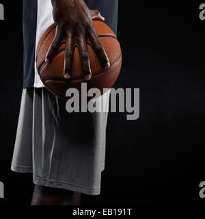 Portrait of a young man holding basketball sur fond noir. Mid section image de joueur de basket-ball de l'Afrique. Banque D'Images