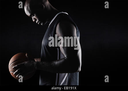 Vue latérale du fit young basketball player holding ball sur fond noir avec l'exemplaire de l'espace. Jouer au basket-ball d'origine afro-américaine Banque D'Images