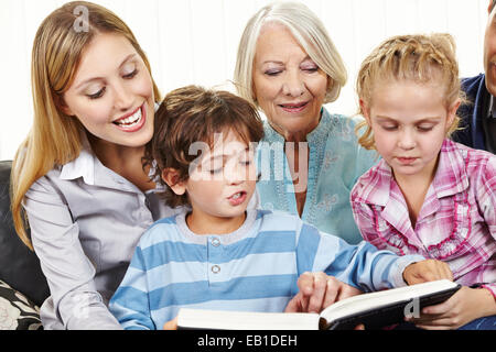 Famille heureuse dans trois générations de lire un livre dans le salon Banque D'Images