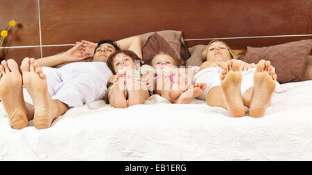 Famille avec deux enfants portant au lit avec leurs pieds en avant Banque D'Images