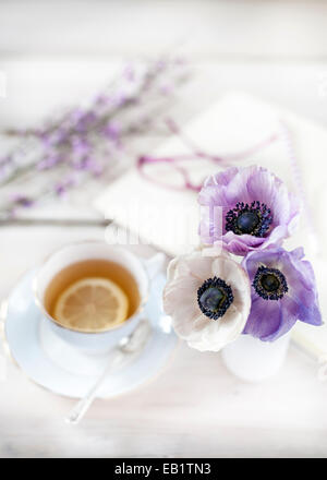 L'heure du thé - thé servi en tasse vintage avec posy d'anémones, bloc-notes et stylo et verres de la toile Banque D'Images