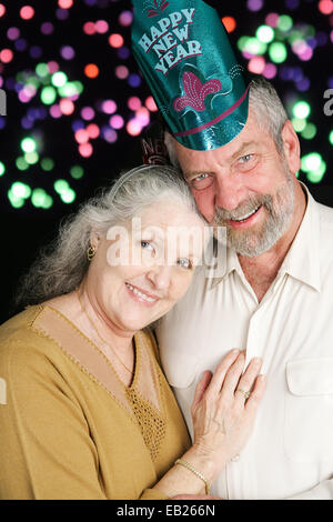Beau couple dans la soixantaine qui pose pour un portrait romantique le soir du Nouvel An. D'artifice en arrière-plan. Banque D'Images