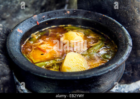 Les aliments africains traditionnels de pommes de terre, le piment et les légumes cuisson dans un pot en argile à la main sur un feu. Banque D'Images