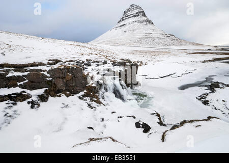 Derrière la montagne Kirkjufell Kirkjufellsfoss cascade gelée dans la neige, Péninsule de Snæfellsnes, l'Islande Banque D'Images