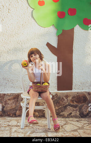 Fille assise sur une chaise avec un panier de pommes Banque D'Images