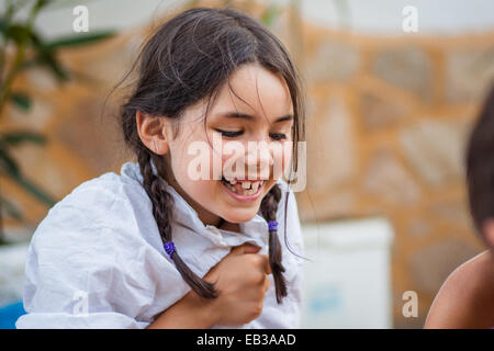 Little girl (6-7) avec tresses et chemise blanche rire heureusement Banque D'Images