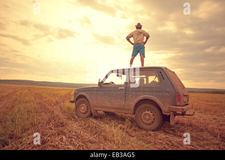 Mari homme debout sur le toit de voiture in rural field Banque D'Images