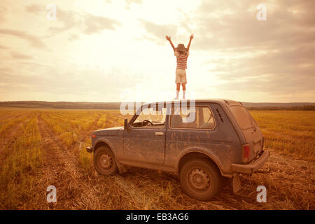 Mari garçon debout sur le toit de voiture in rural field Banque D'Images