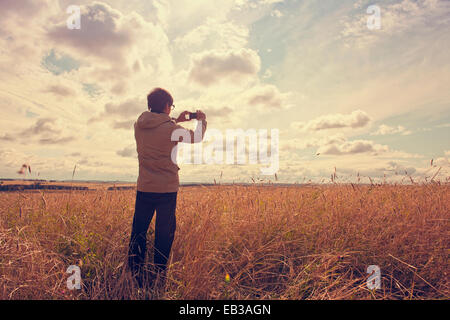 Mari man photographing rural field with cell phone Banque D'Images