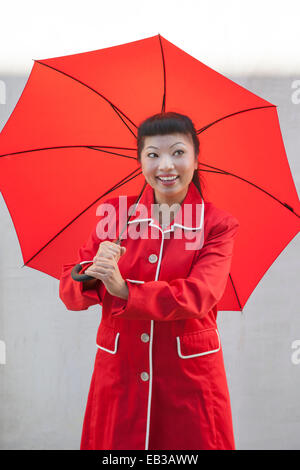 Femme avec parapluie ouvert porte manteau rouge Banque D'Images