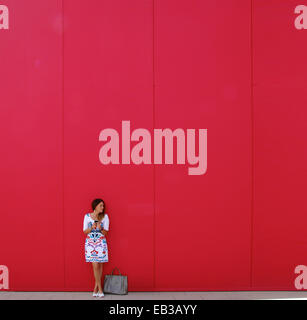 Femme debout à côté de son sac à main devant un message texte mural rouge Banque D'Images