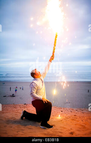 Caucasian man holding d'artifice sur la plage Banque D'Images