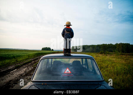 Caucasian boy standing sur toit de voiture in rural field Banque D'Images