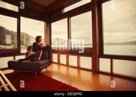 Mixed Race woman looking out window of modern house Banque D'Images