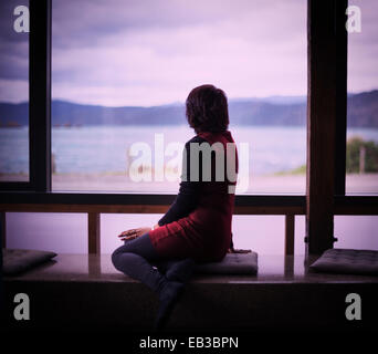 Mixed Race woman looking out window of modern house Banque D'Images