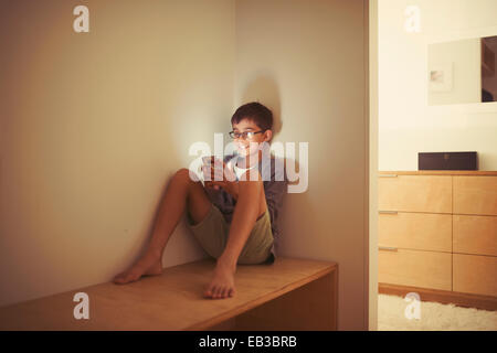 Mixed Race boy using cell phone on bench Banque D'Images