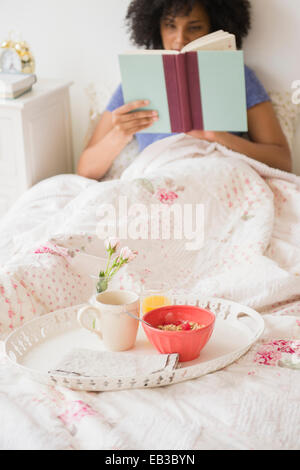 Woman Reading book et avec petit-déjeuner au lit Banque D'Images