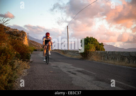 Homme en vélo le long d'une route côtière au coucher du soleil, Corse, France Banque D'Images