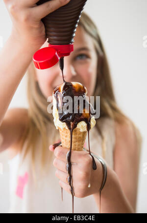 Messy Caucasian girl pouring sirop de chocolat sur ice cream cone Banque D'Images