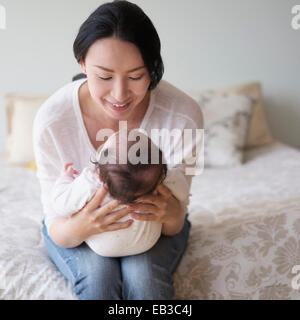 Asian mother holding baby on bed
