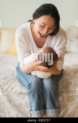 Asian mother holding baby on bed Banque D'Images