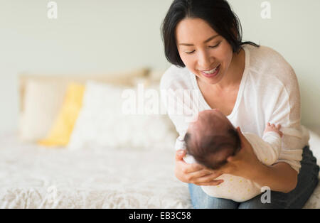 Asian mother holding baby on bed Banque D'Images