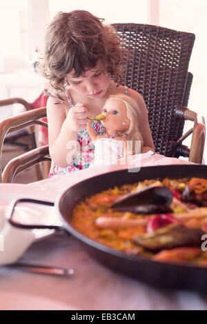 Girl sitting at dinner table prétendant pour nourrir sa poupée Banque D'Images