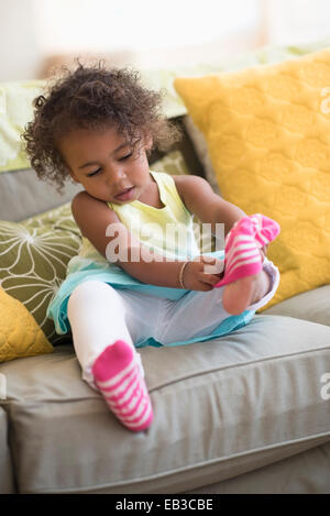 Mixed Race girl tirant sur les chaussettes dans la salle de séjour Banque D'Images