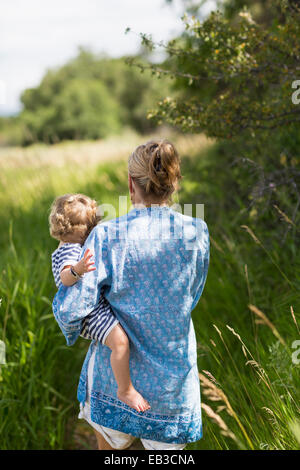 Caucasian mother carrying baby son in grassy field Banque D'Images