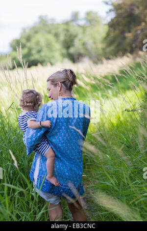 Caucasian mother carrying baby son in grassy field Banque D'Images