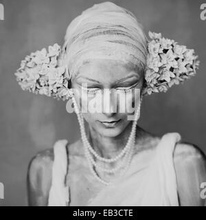 Portrait of young woman wearing composent, greasepaint, perles, et décorations de l'oreille de l'inflorescence ressemblant Banque D'Images