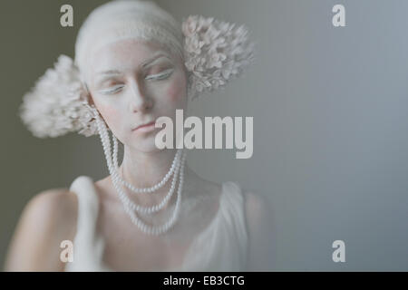 Portrait of young woman wearing composent, greasepaint, perles, et décorations de l'oreille de l'inflorescence ressemblant avec les yeux fermé Banque D'Images