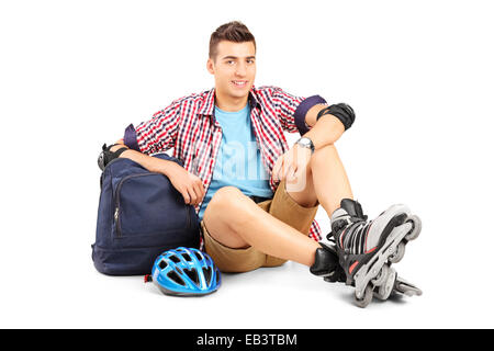 Jeune homme avec du roller assis sur le plancher isolé sur fond blanc Banque D'Images